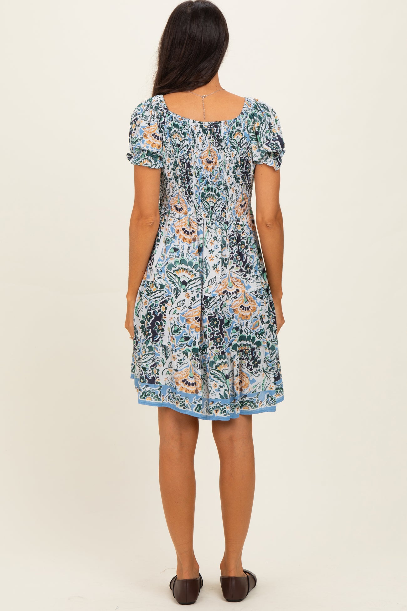 woman wearing a blue and green floral print short puff sleeve dress, showing the back view