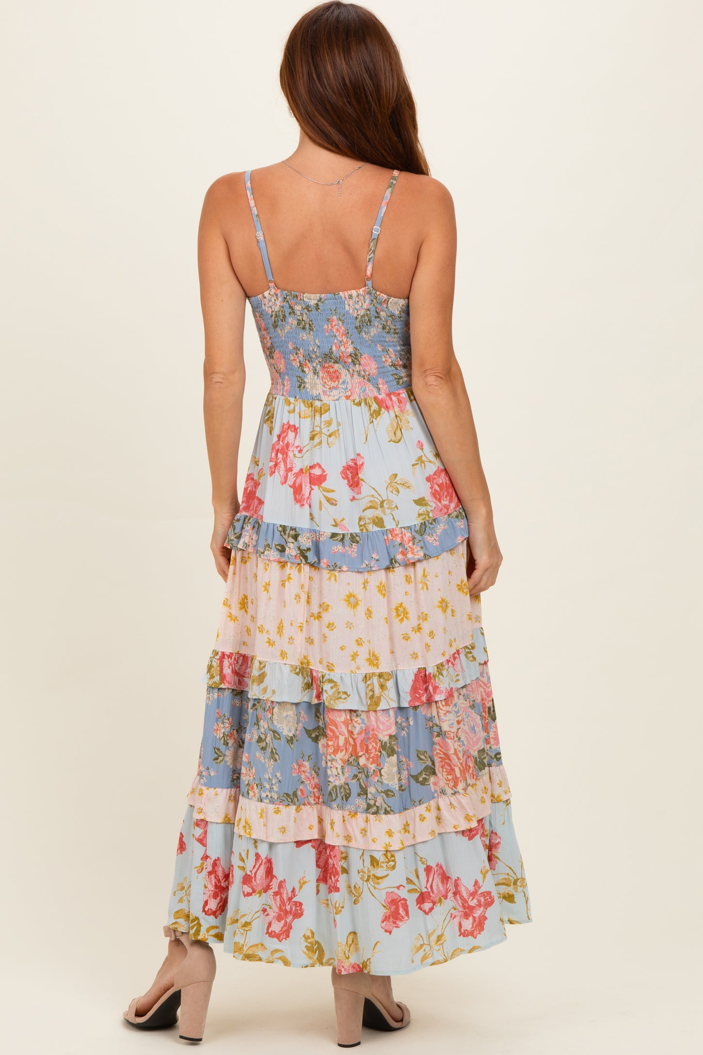 woman wearing a floral tiered maxi dress with a light blue background and spaghetti straps, viewed from the back