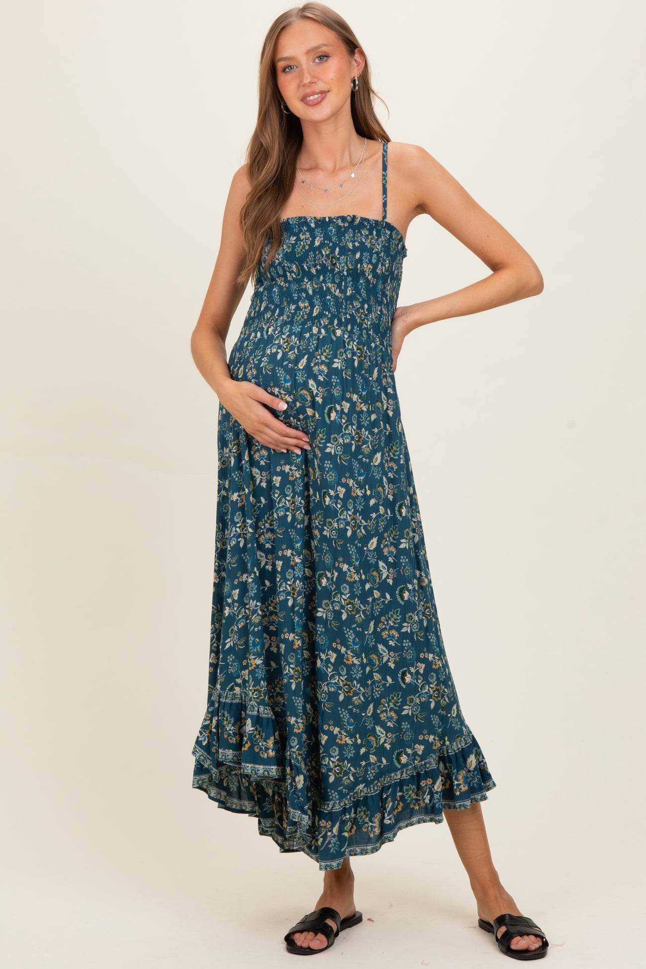 woman wearing a teal maternity maxi dress with floral print and a gathered bodice, holding her baby bump