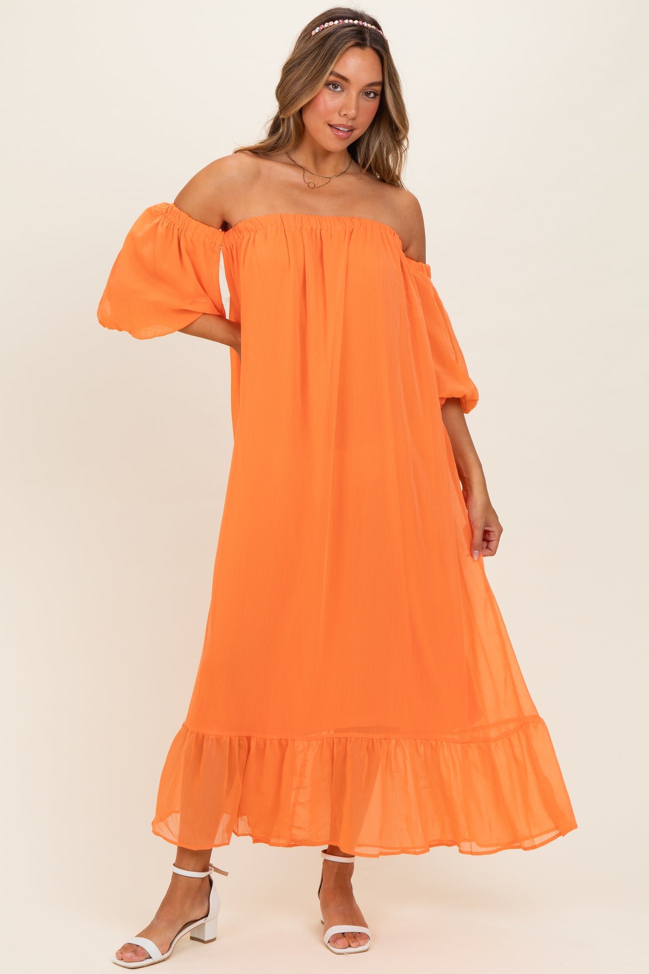 woman wearing a vibrant orange off-the-shoulder maxi dress with puffed sleeves and a ruffled hemline