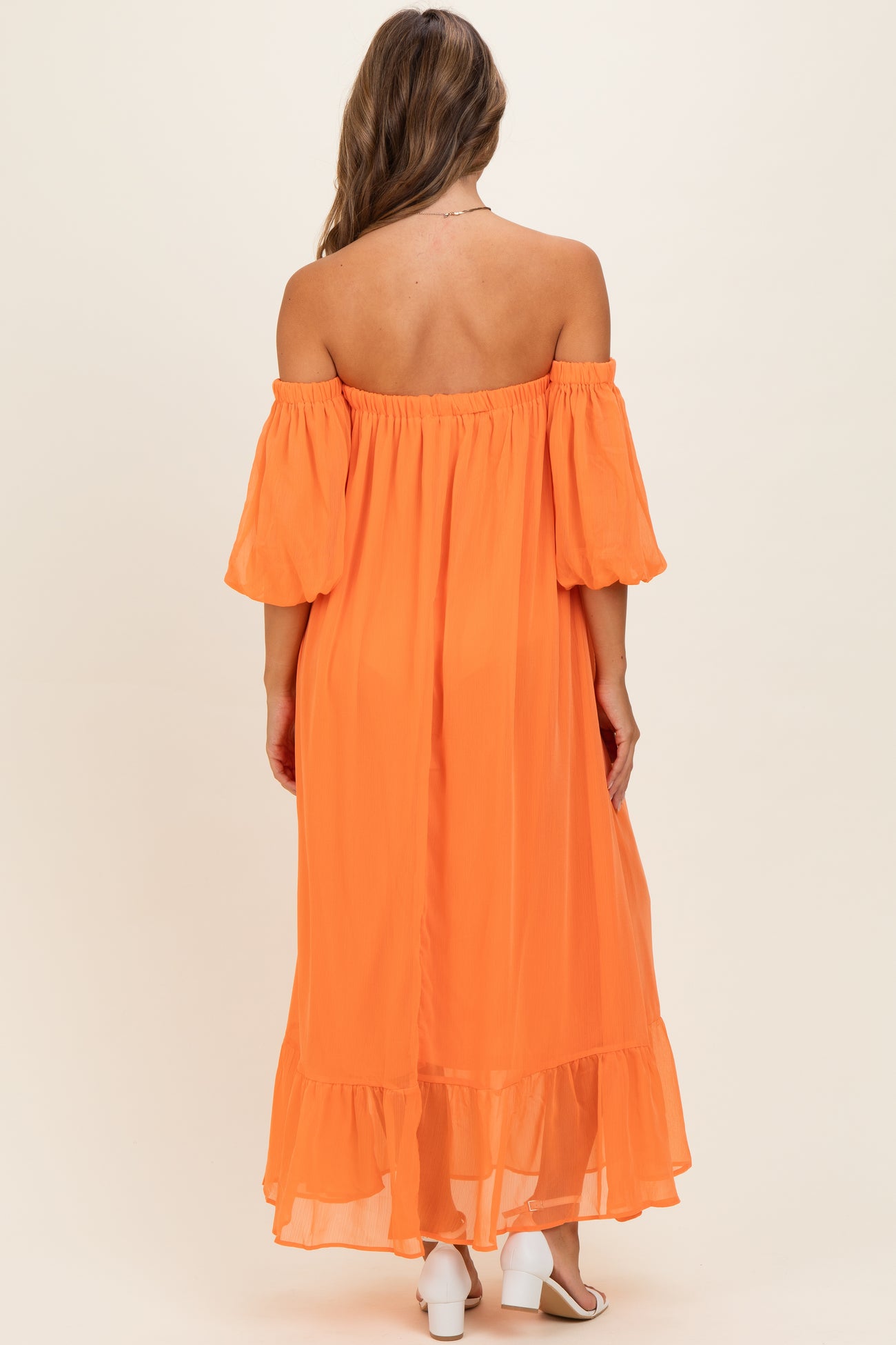 woman wearing an off-shoulder orange maxi dress with puff sleeves and a ruffled hem