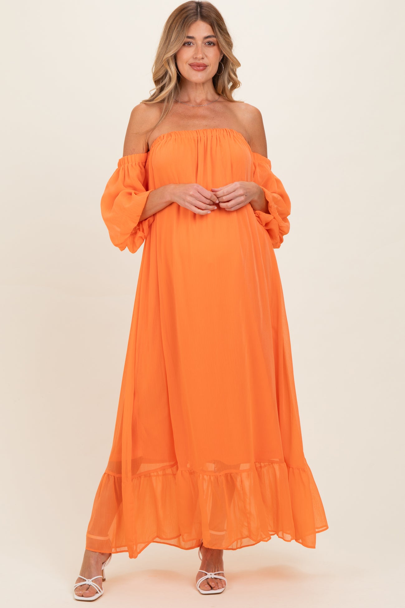 woman wearing a vibrant orange off-the-shoulder maternity dress with puff sleeves and a ruffled hemline