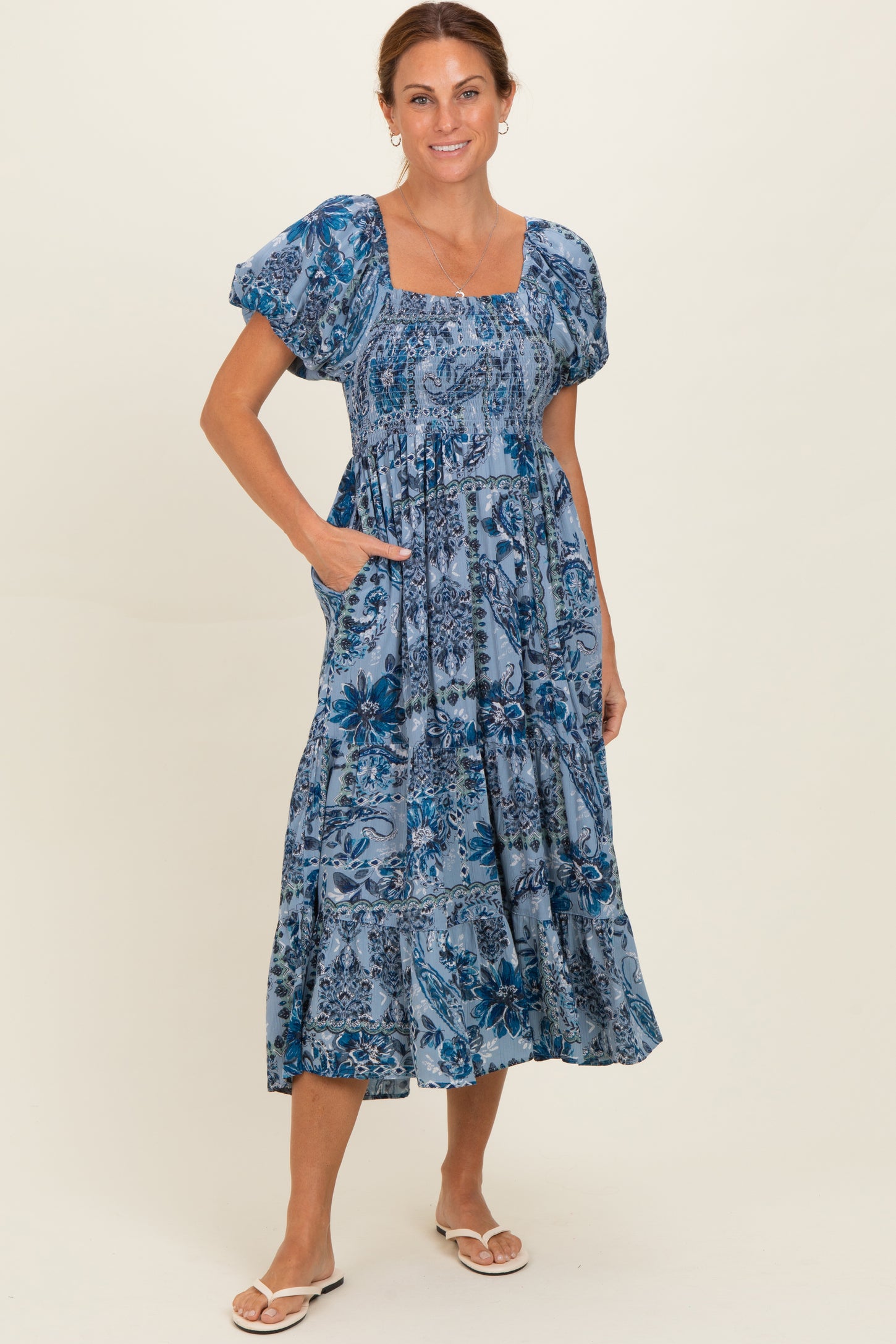 woman wearing a blue floral print midi dress with puff sleeves and pockets, standing on a light background