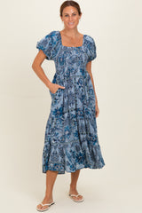woman wearing a blue floral print midi dress with puff sleeves and pockets, standing on a light background