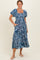 woman wearing a blue floral print midi dress with puff sleeves and pockets, standing on a light background