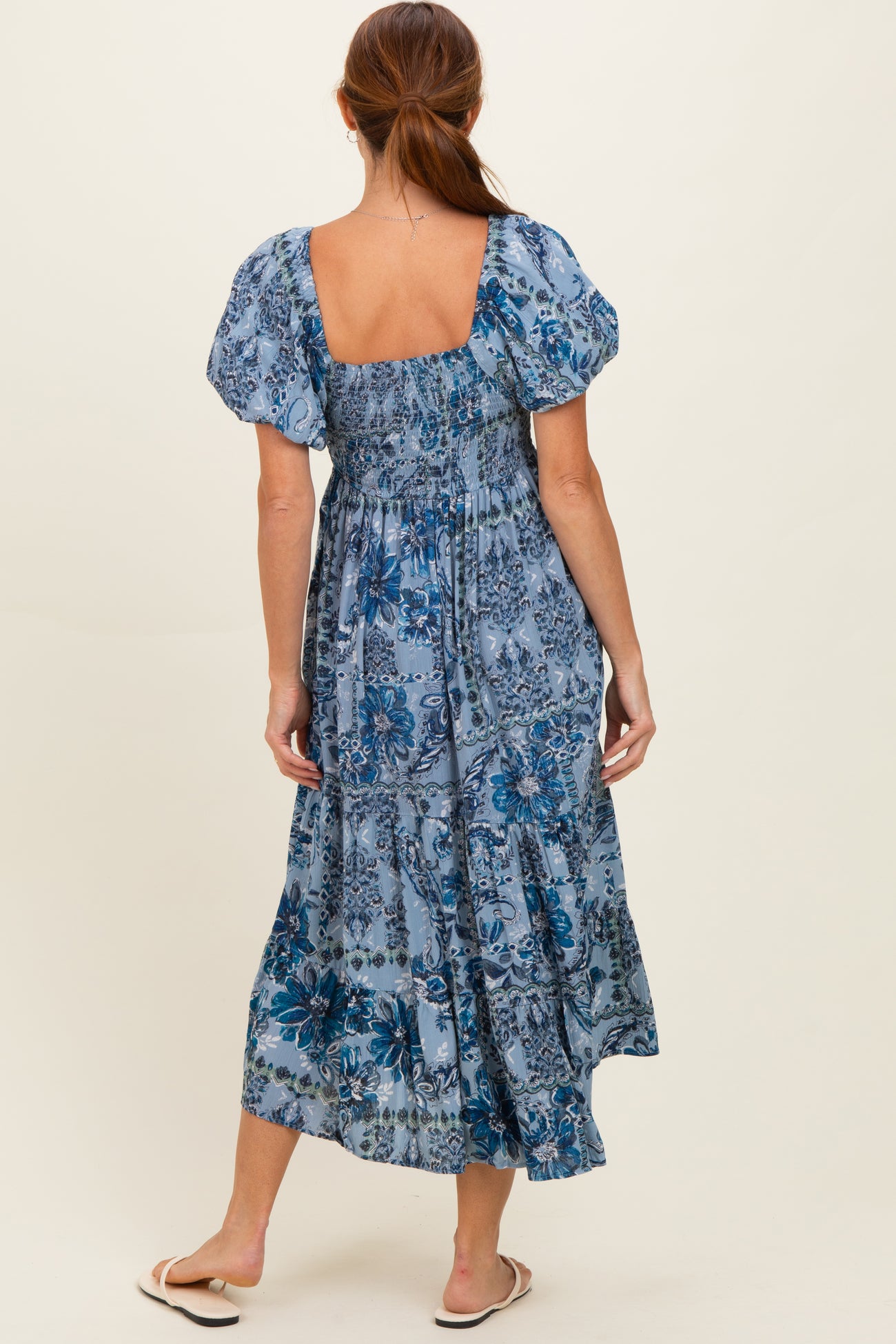 woman wearing a blue floral puff sleeve maxi dress, showcasing a smocked back and tiered skirt