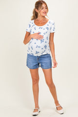 woman wearing a floral print maternity top and denim shorts while holding her baby bump