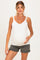 woman wearing a white maternity tank top with lace trim and holding her baby bump, paired with gray shorts