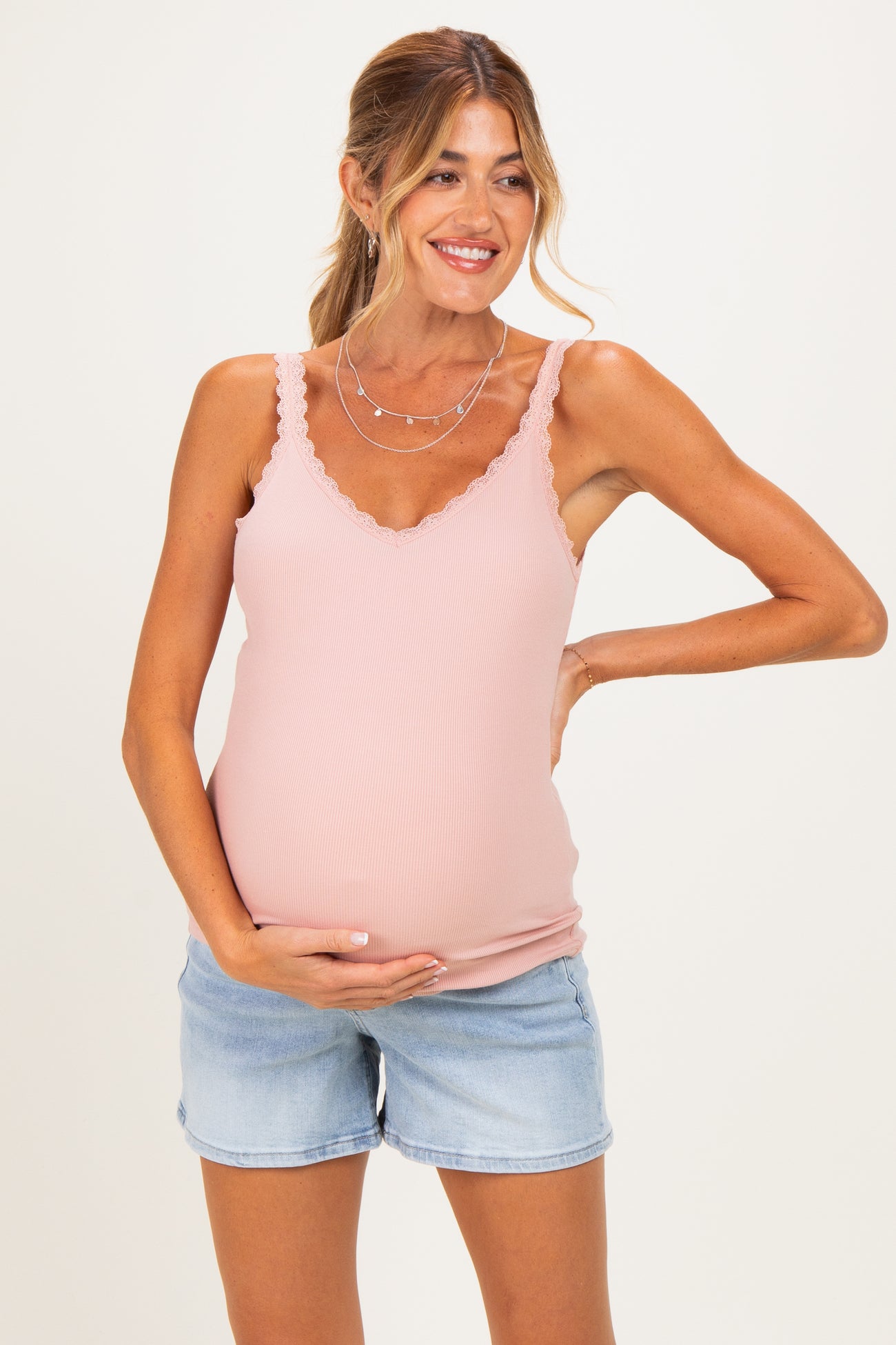 woman wearing a light pink maternity tank top with scalloped edges and denim shorts, showing her baby bump