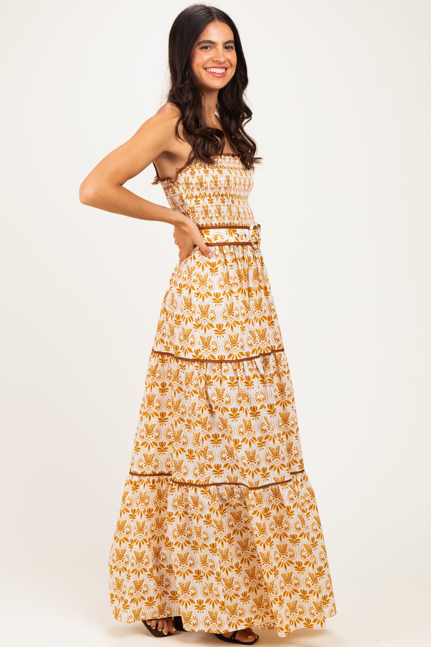woman wearing a white maxi dress with orange floral print and a smocked bodice, posing with hands on her hips