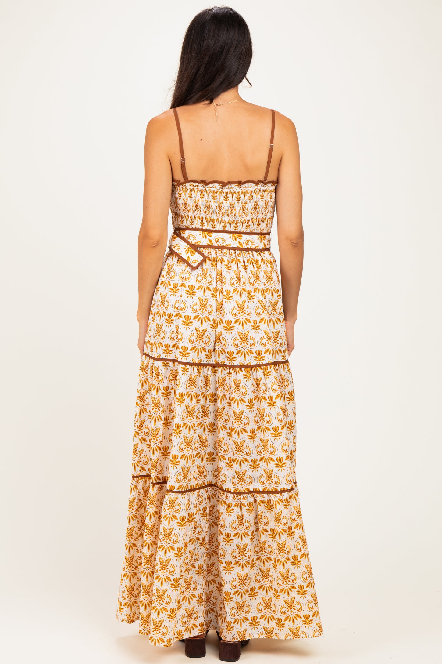 woman wearing a back view of a white and orange floral maxi dress with adjustable straps and a tiered skirt
