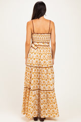 woman wearing a back view of a white and orange floral maxi dress with adjustable straps and a tiered skirt