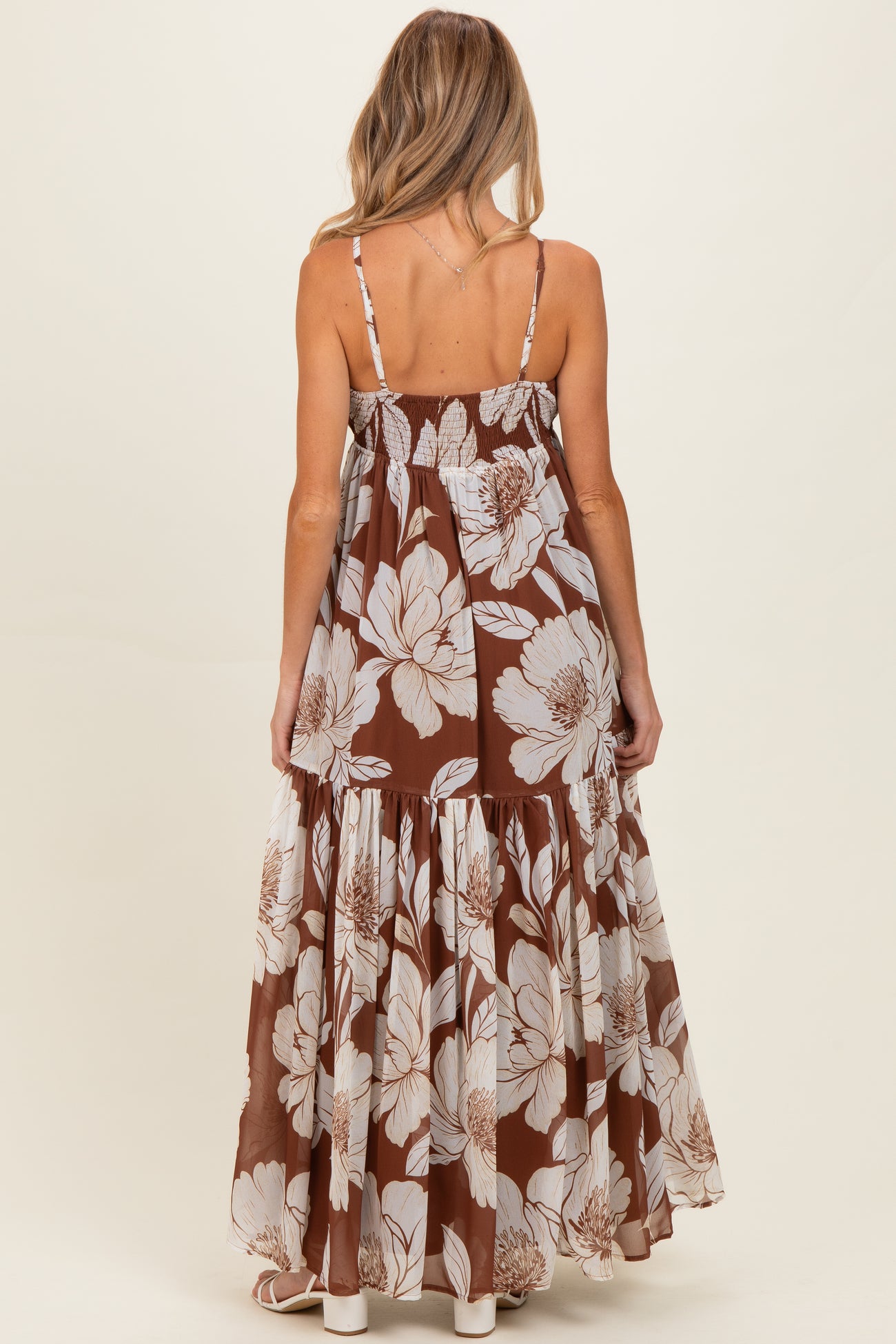 woman wearing a brown floral print maternity maxi dress with a tiered skirt and adjustable straps, showing her baby bump