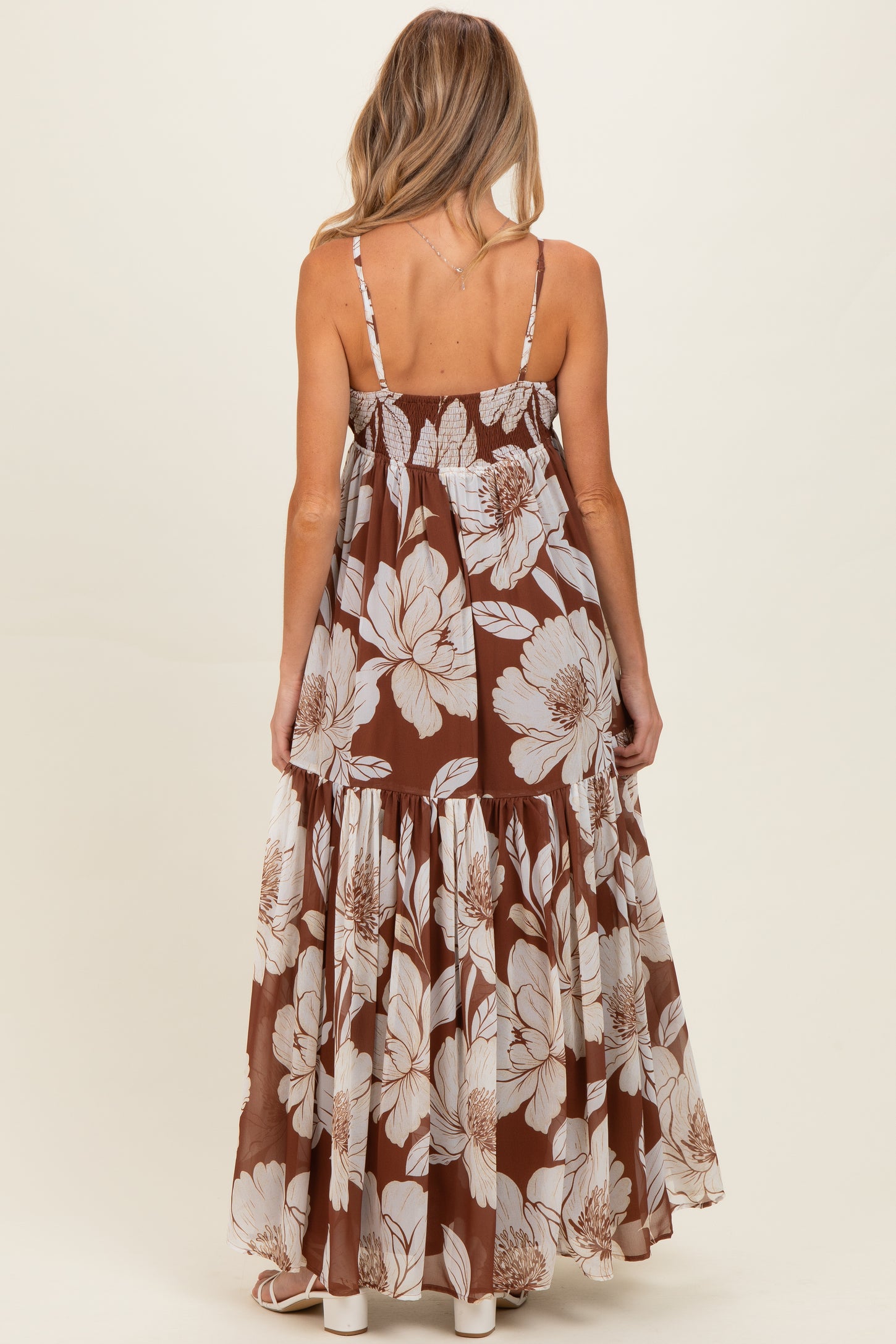 woman wearing a brown floral print maternity maxi dress with a tiered skirt and adjustable straps, showing her baby bump