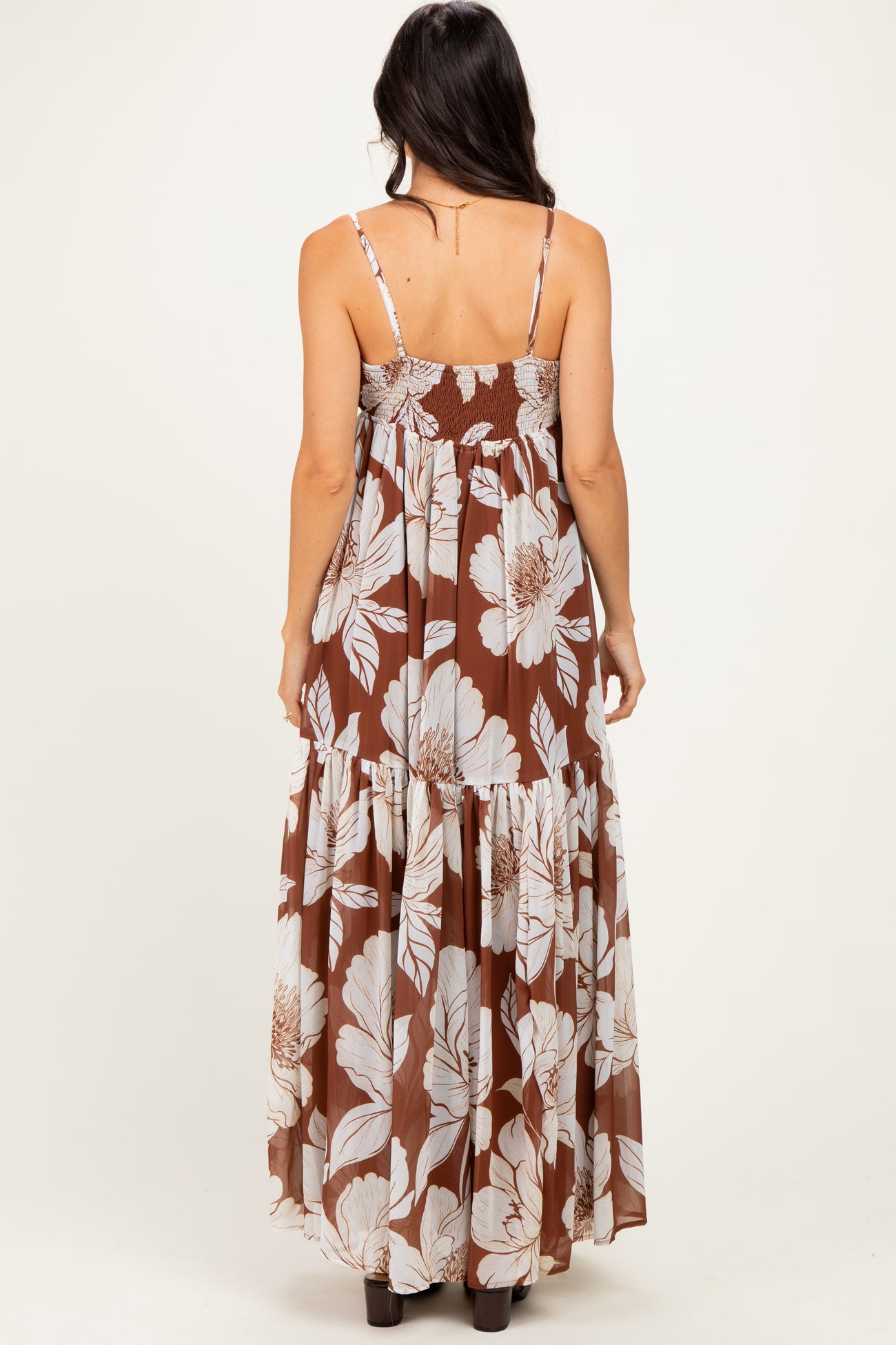 woman wearing a brown floral maxi dress with adjustable spaghetti straps and tiered skirt, shown from the back
