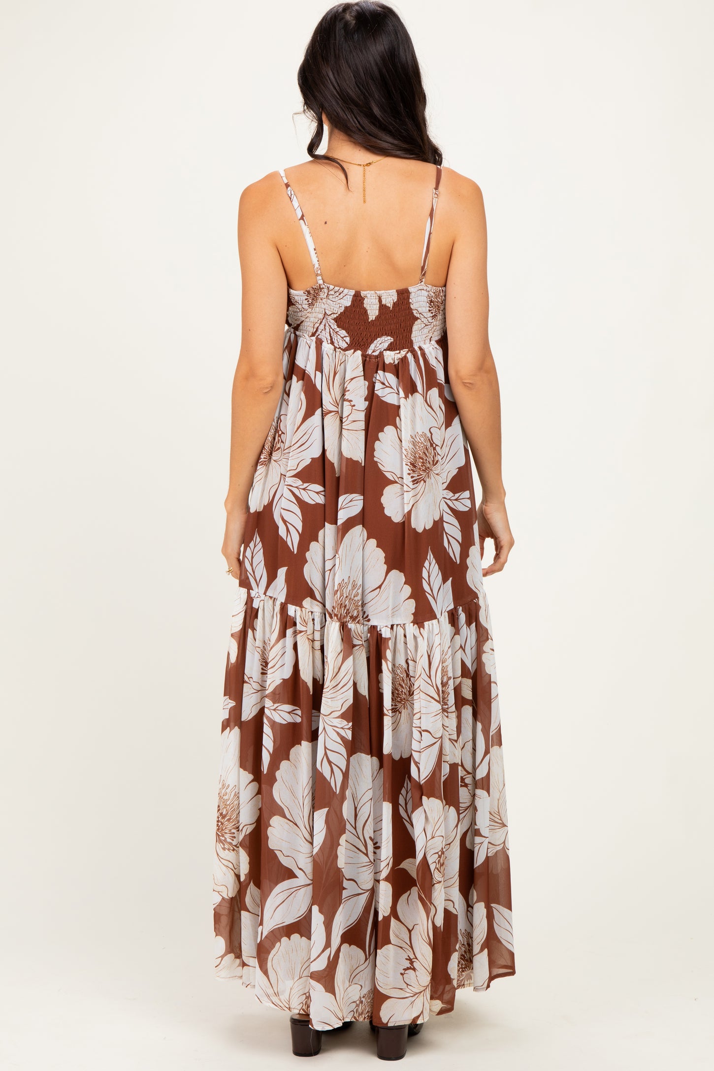 woman wearing a brown floral maxi dress with adjustable spaghetti straps and tiered skirt, shown from the back