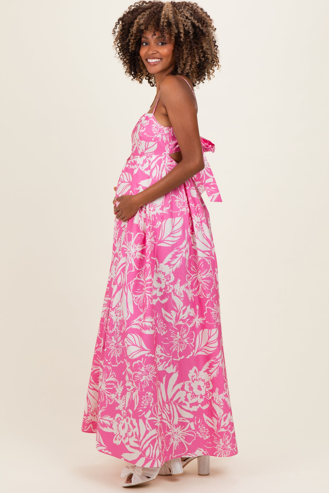 woman wearing a pink floral maternity maxi dress with a bow detail, showcasing her baby bump