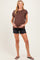 woman wearing a brown short sleeve maternity top and black distressed shorts, holding her baby bump