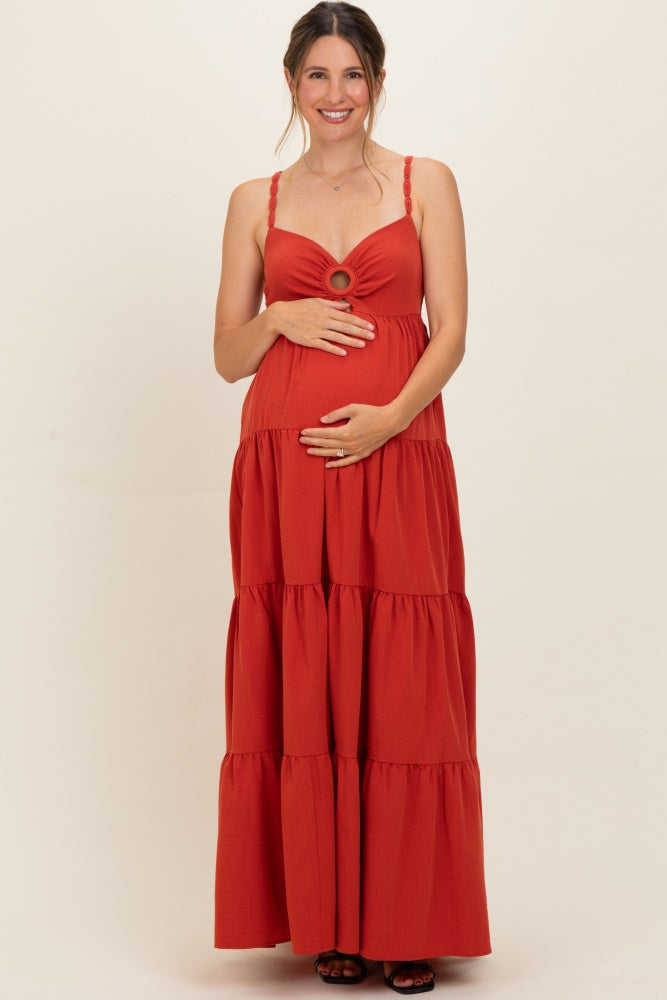 woman wearing a rust red maternity maxi dress with tiered design and a circular detail at the bust, holding her baby bump