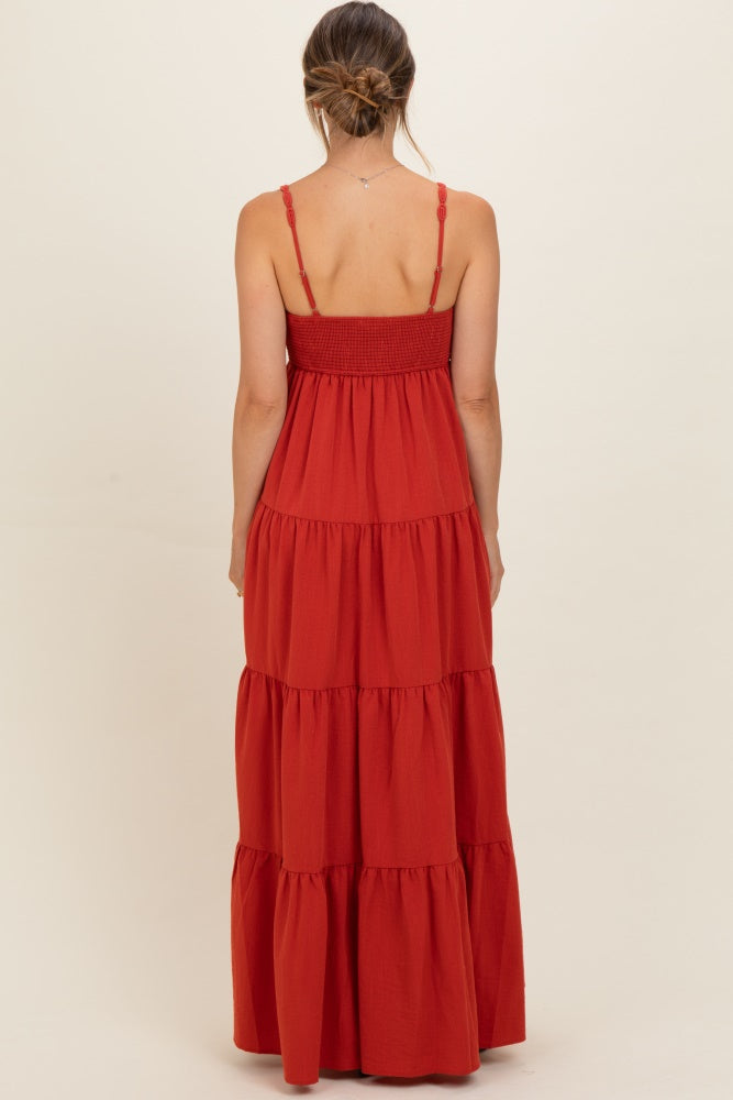 woman wearing a rust red tiered maxi maternity dress with adjustable straps and smocked bodice