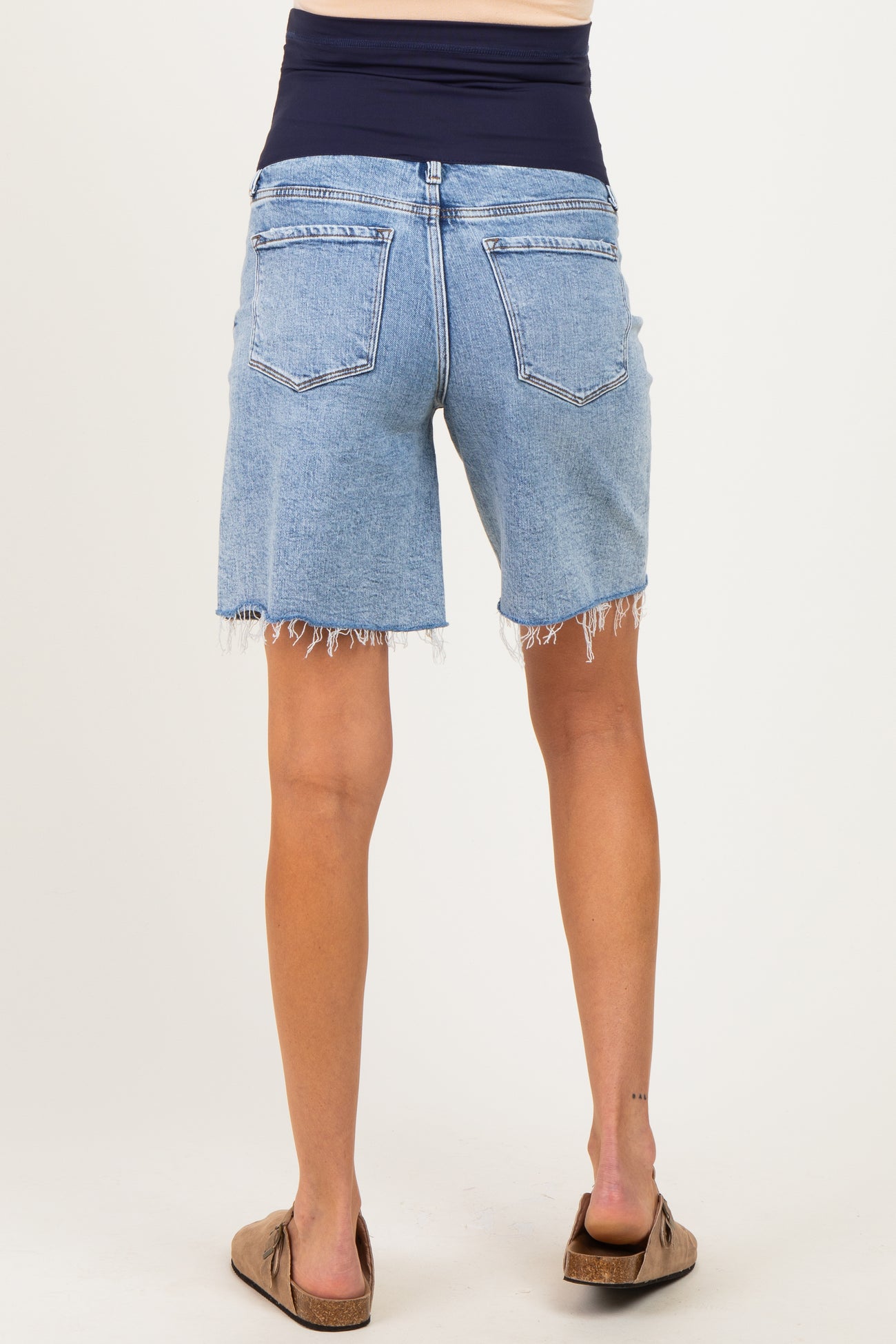 woman wearing light blue denim maternity shorts with a wide black waistband and frayed hems, seen from the back