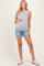 woman wearing a gray sleeveless maternity tank top and holding her baby bump, paired with denim shorts and white sneakers