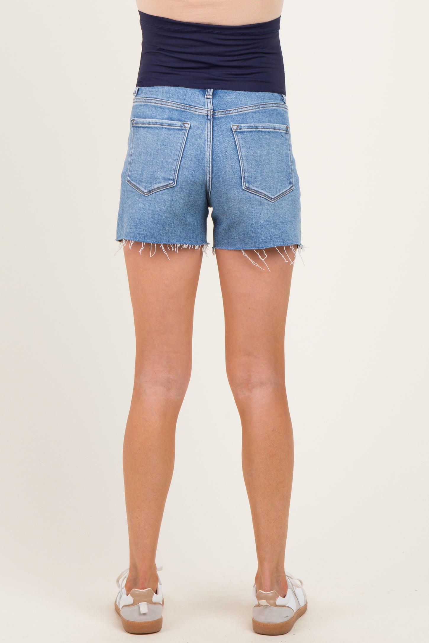 woman wearing a pair of light blue denim maternity shorts with frayed hem, showing her back view
