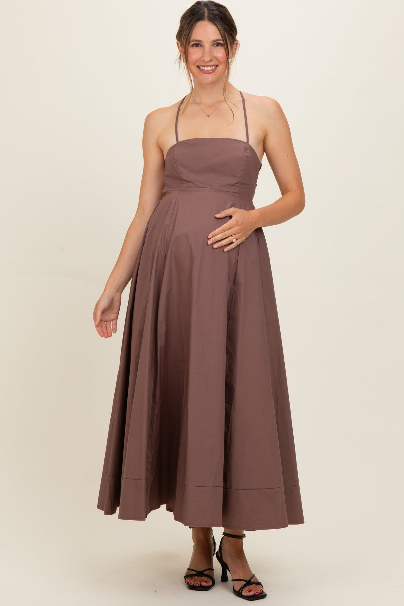 woman wearing a brown strapless maternity gown with a flowing skirt and holding her baby bump