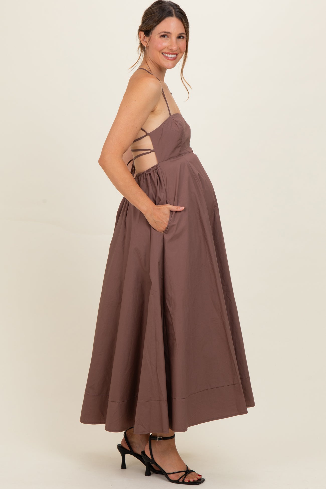 woman wearing a brown sleeveless maternity dress with a flowy skirt and side pockets, showcasing her baby bump