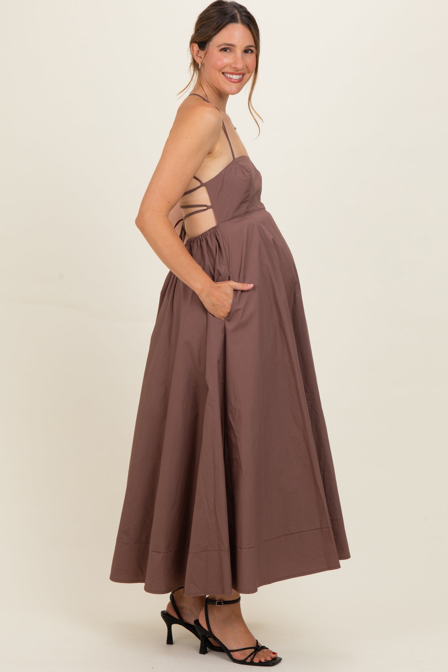 woman wearing a brown sleeveless maternity dress with a flowy skirt and side pockets, showcasing her baby bump