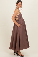 woman wearing a brown sleeveless maternity dress with a flowy skirt and side pockets, showcasing her baby bump