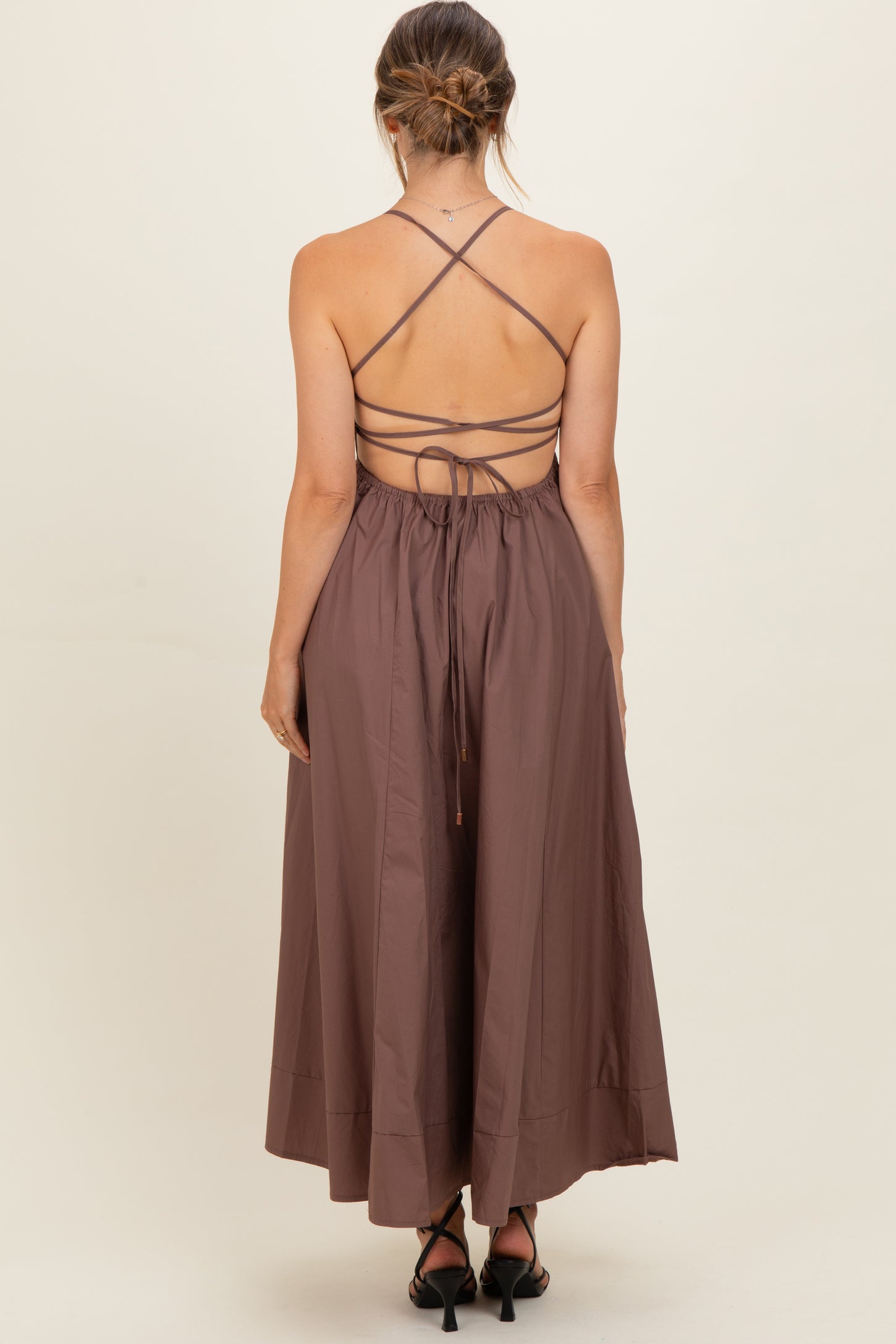 woman wearing a brown backless maternity dress with crisscross straps and a flowy skirt