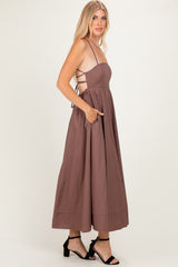 woman wearing a sleeveless brown maxi dress with a fitted bodice and open back, featuring pockets and strappy details