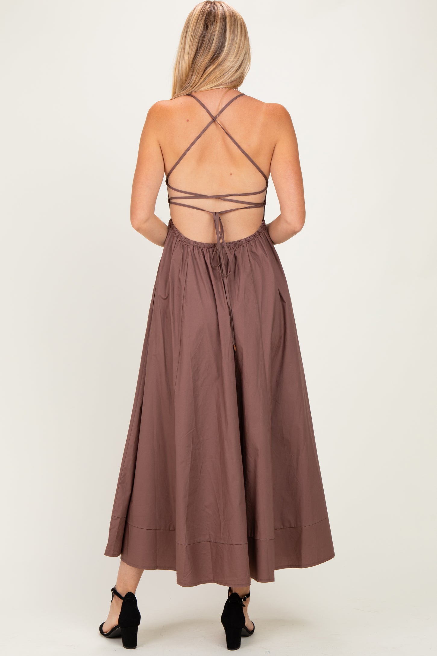 woman wearing a brown maxi dress with a crisscross back and tie details, viewed from the back