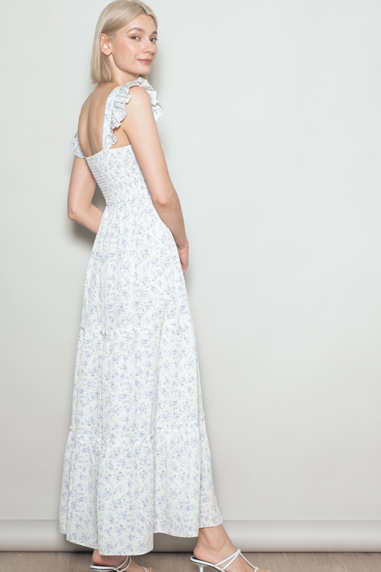 woman wearing a white floral maxi dress with ruffled straps, standing sideways against a light background