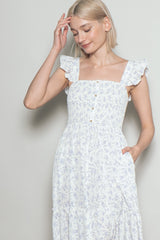 woman wearing a white floral print maxi dress with ruffled shoulder straps and a square neckline