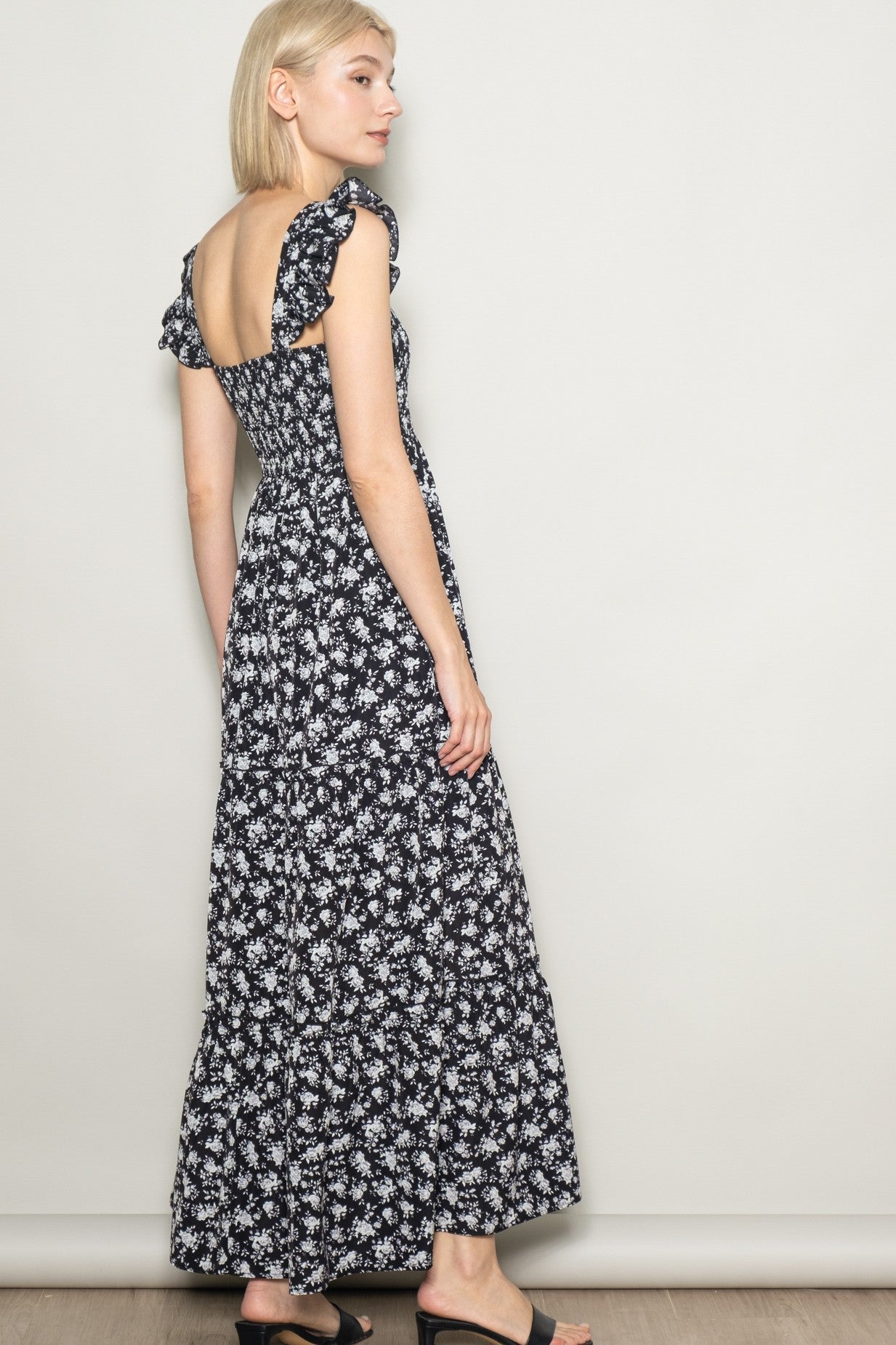 woman wearing a black and white floral maxi dress with ruffled sleeves and an open back, standing sideways