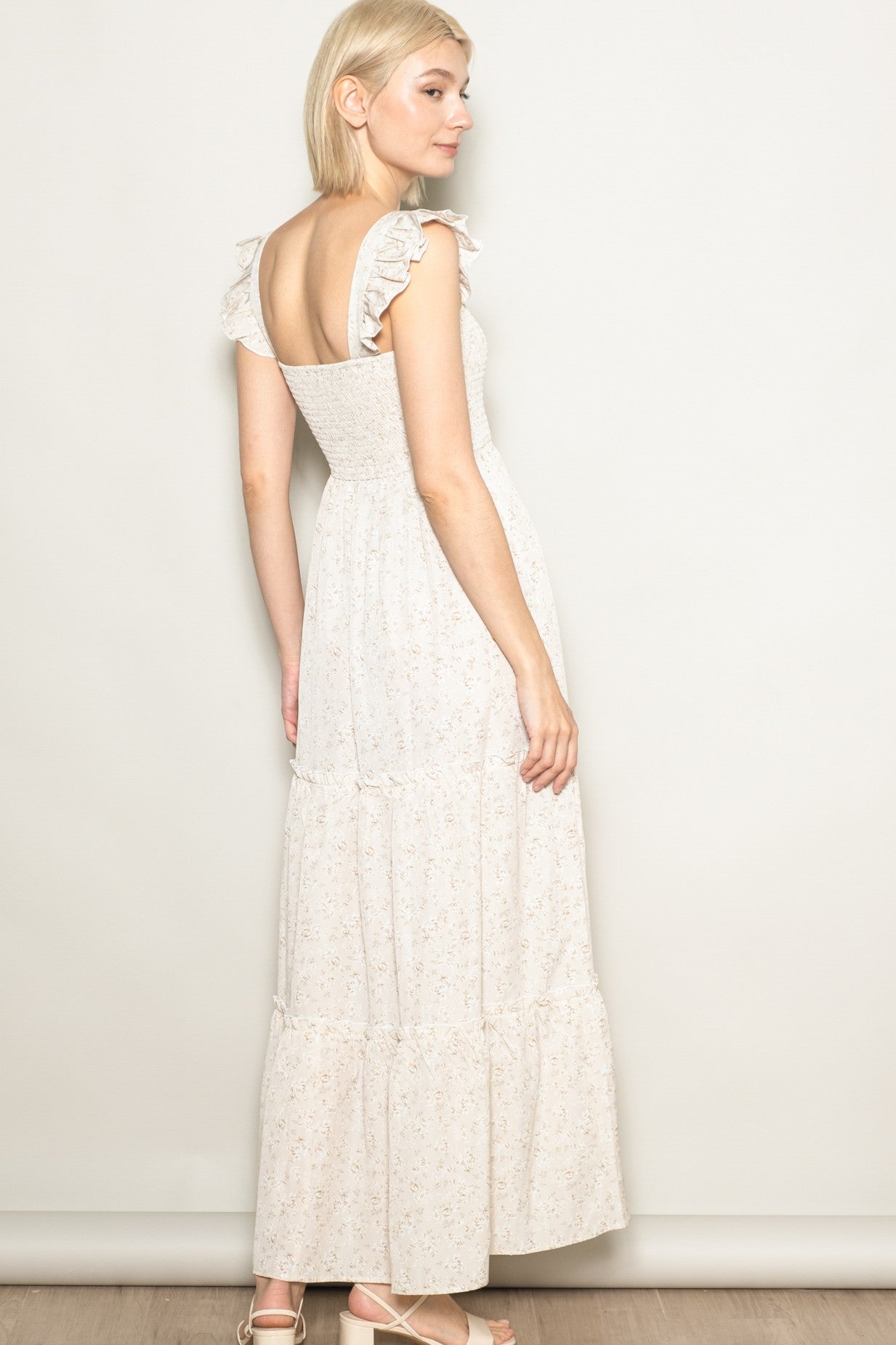 woman wearing a light beige floral maxi dress with ruffled straps and a tiered skirt, shown from the back