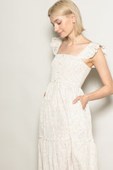 woman wearing a cream floral print maxi dress with ruffled straps and a smocked bodice, hands in pockets