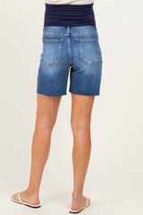 woman wearing dark wash maternity denim shorts with a rolled hem and a stretchy waistband, standing with feet crossed