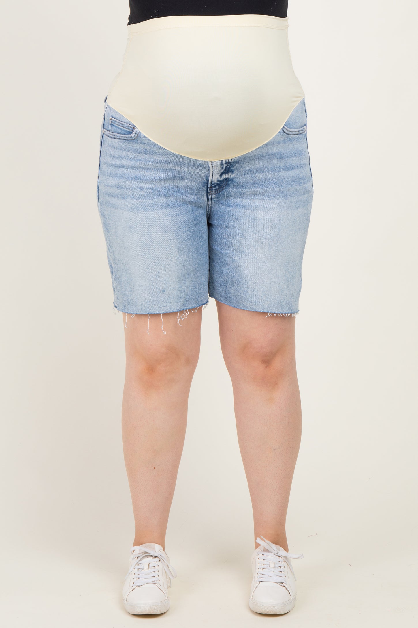 woman wearing light blue denim maternity shorts with a supportive beige belly band, styled with white sneakers