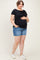 woman wearing a black short sleeve maternity top and denim shorts, holding her baby bump