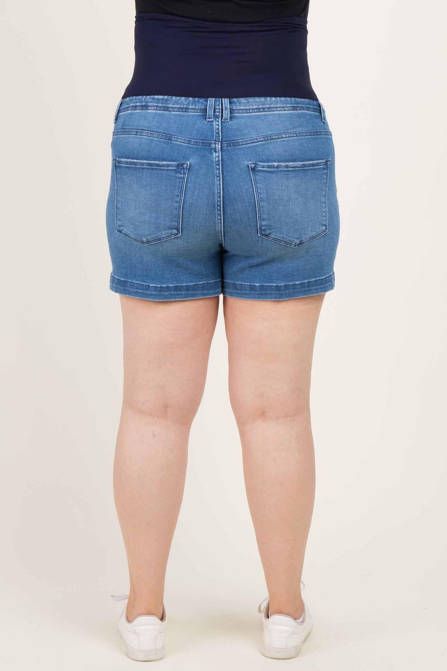 woman wearing a pair of blue maternity plus denim shorts, showing the back view with a supportive waistband
