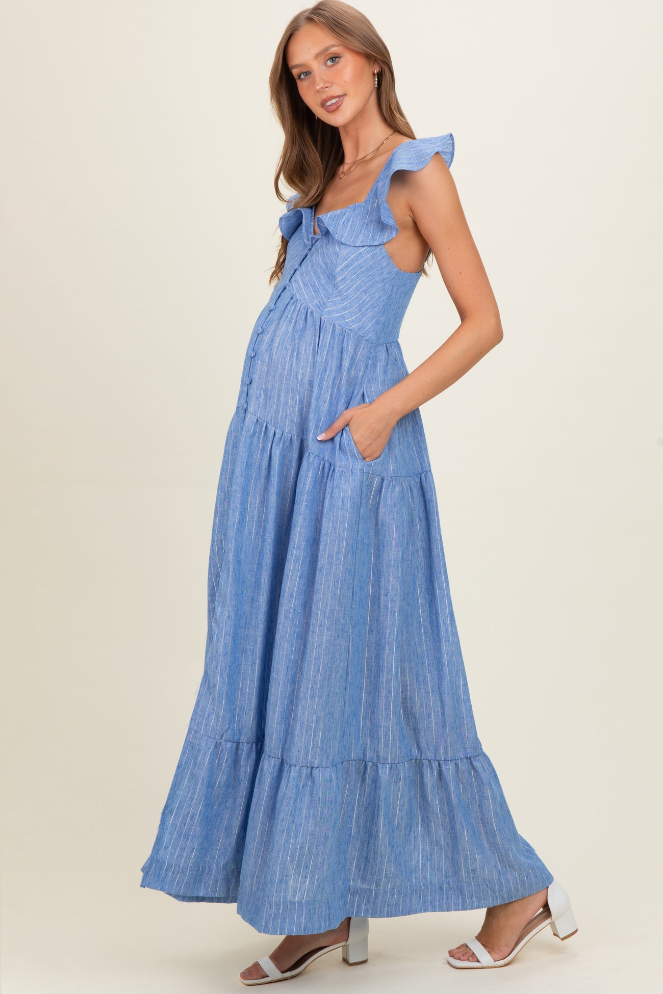 woman wearing a blue striped maternity maxi dress with ruffled straps and pockets, showcasing a baby bump