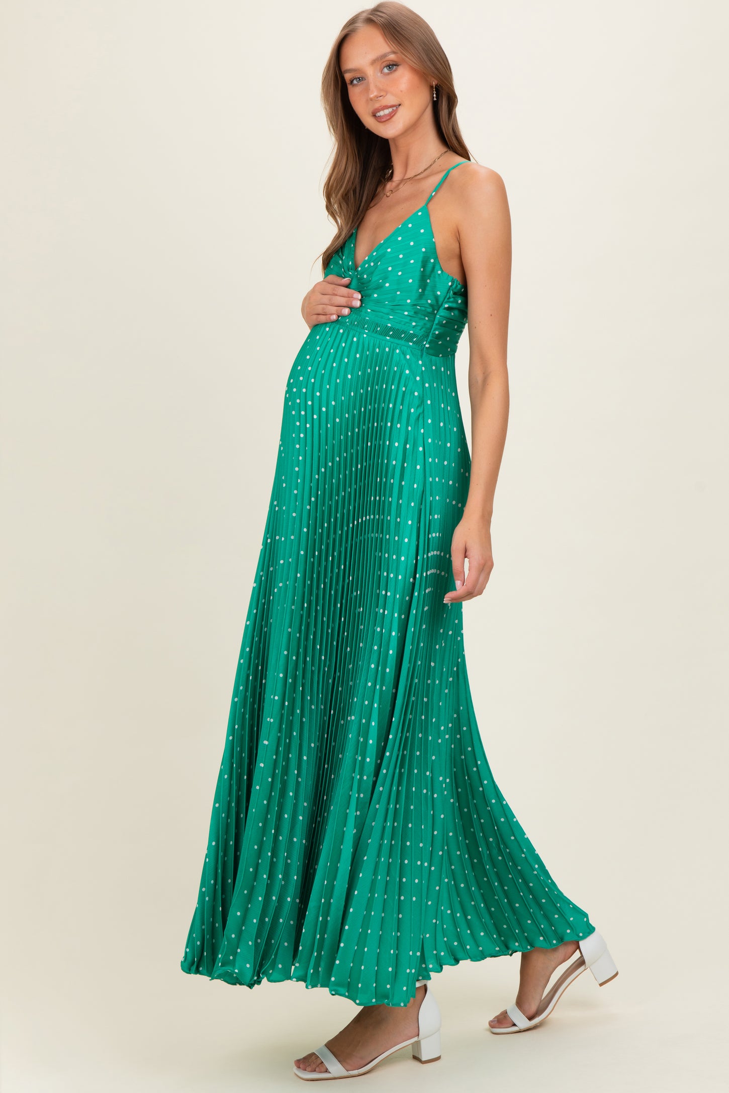 woman wearing a green pleated maternity dress with white polka dots and a visible baby bump
