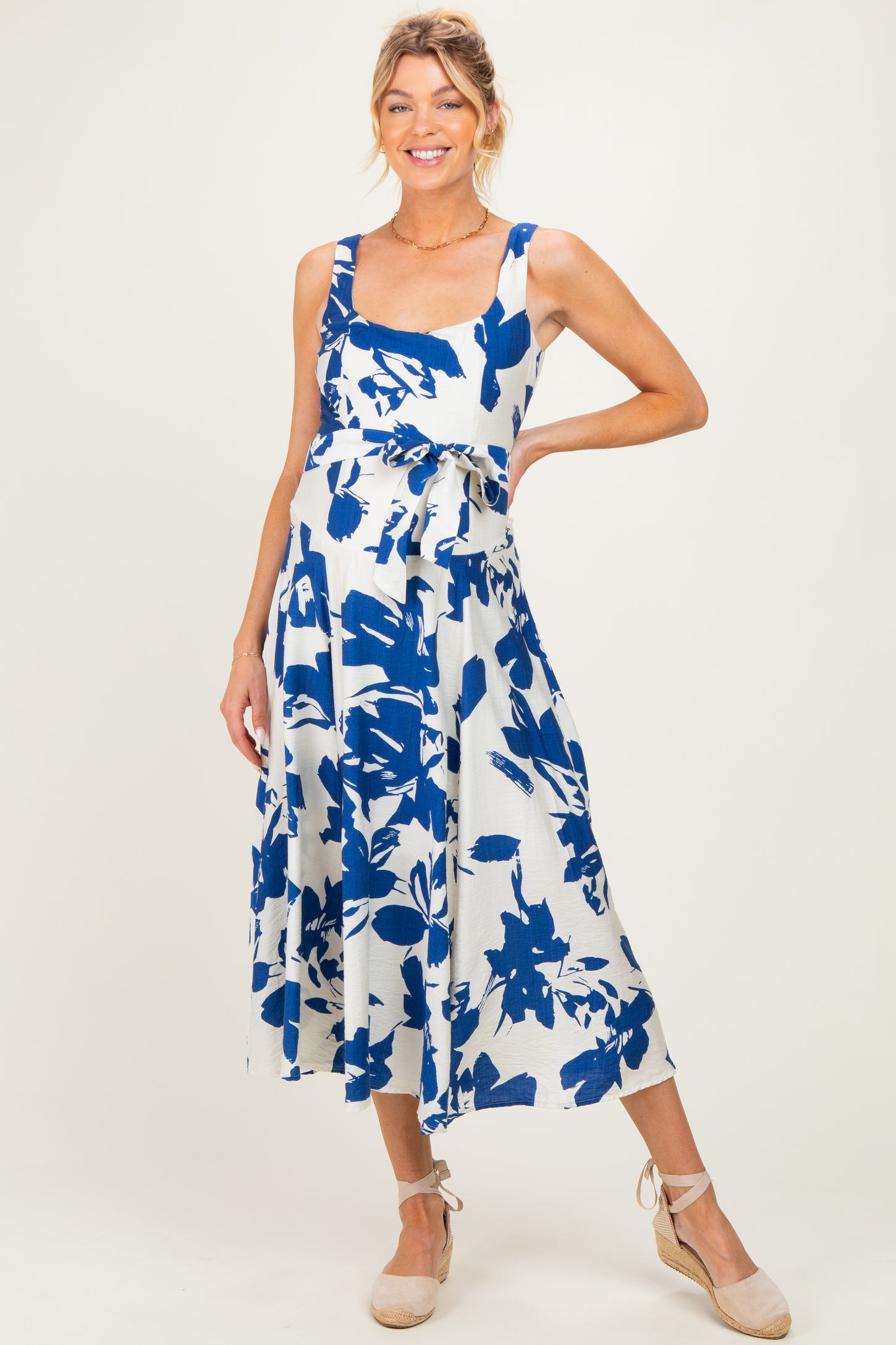 woman wearing a blue and white floral maternity dress with a tie waist and a flowing skirt, showcasing her baby bump