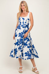 woman wearing a white sleeveless midi dress with a blue floral print and a tied waist, paired with wedge sandals
