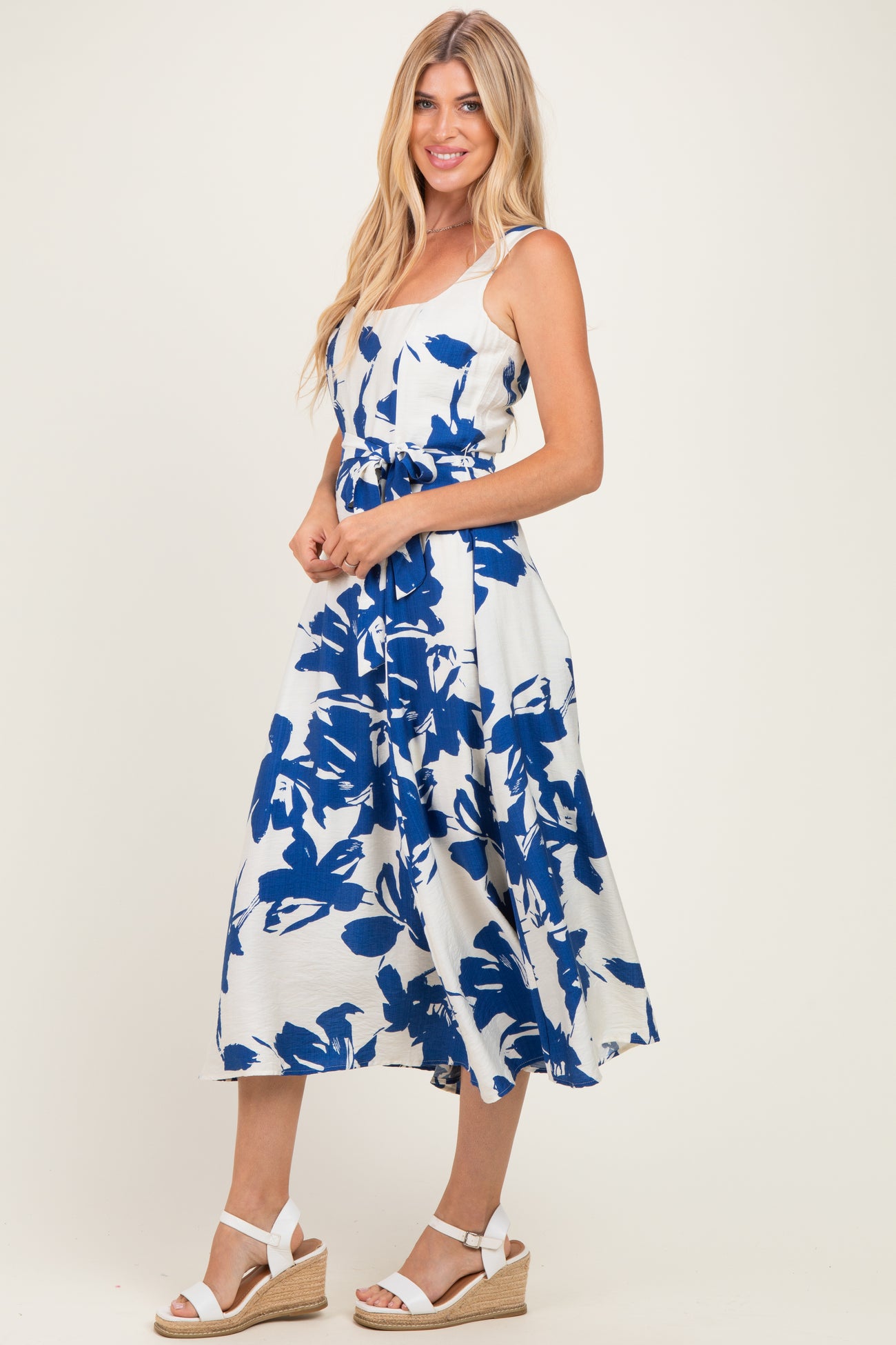 woman wearing a white midi dress with blue floral print, standing in espadrille wedges
