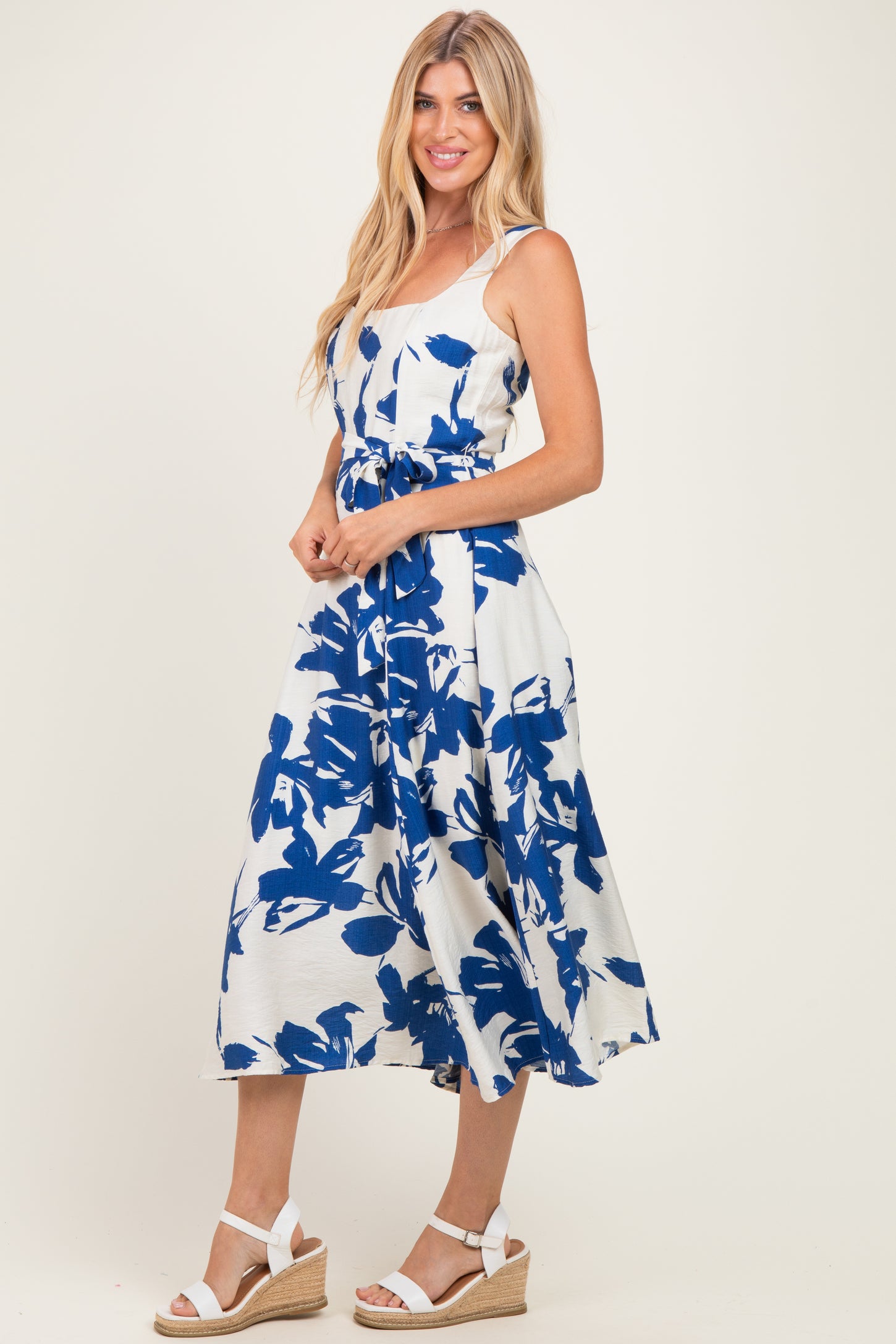 woman wearing a white midi dress with blue floral print, standing in espadrille wedges