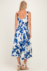 woman wearing a backless white dress with blue floral print and a flowy midi skirt, standing on a light background